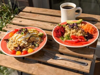 Two plates of colorful plated food on an outside table with a cup of coffee at Daily Beets in Downtown, New Orleans